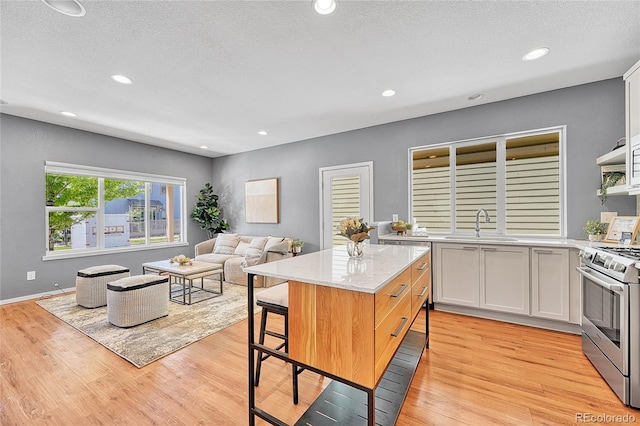1903 W 66th Ave, Denver, CO 80221 - kitchen with stainless steel gas range, light wood-style floors, recessed lighting, a kitchen island, and light stone counters