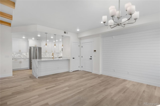 unfurnished living room with a chandelier, light wood finished floors, a sink, and visible vents