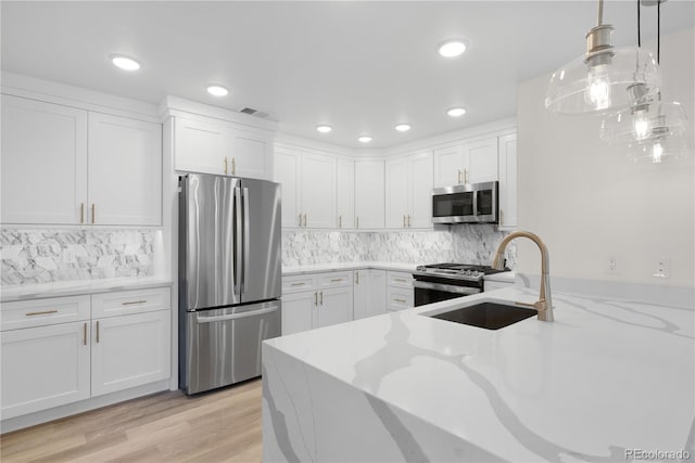 kitchen with stainless steel appliances, white cabinetry, a sink, and light stone countertops