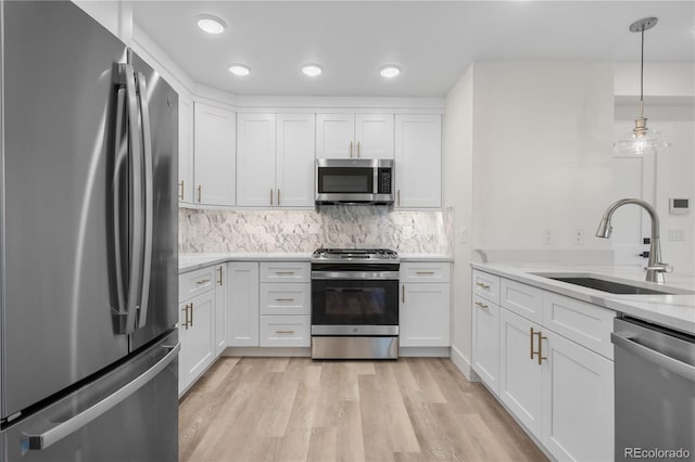 kitchen with light wood-style flooring, a sink, white cabinets, appliances with stainless steel finishes, and tasteful backsplash