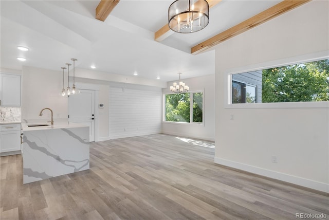 unfurnished living room with baseboards, beamed ceiling, an inviting chandelier, light wood-style floors, and a sink