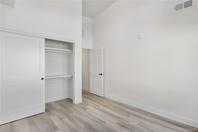 unfurnished bedroom with baseboards, visible vents, a towering ceiling, wood finished floors, and a closet