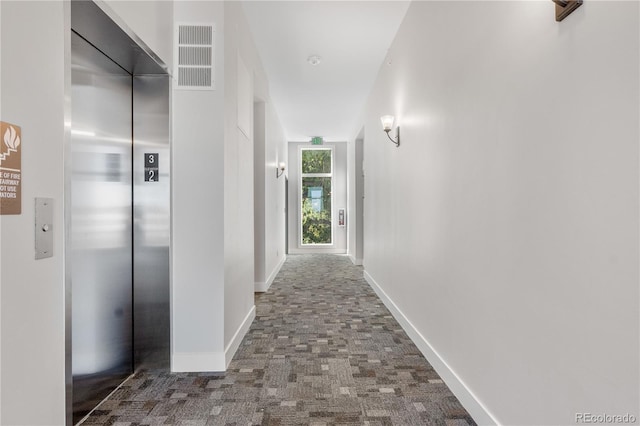 hallway featuring carpet floors, elevator, visible vents, and baseboards