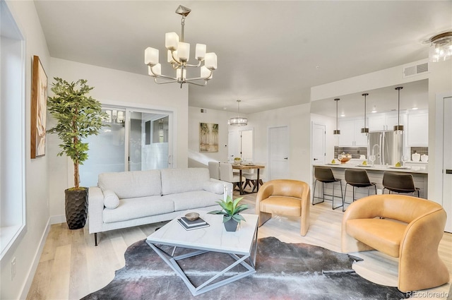 living area with light wood-style floors, visible vents, and an inviting chandelier