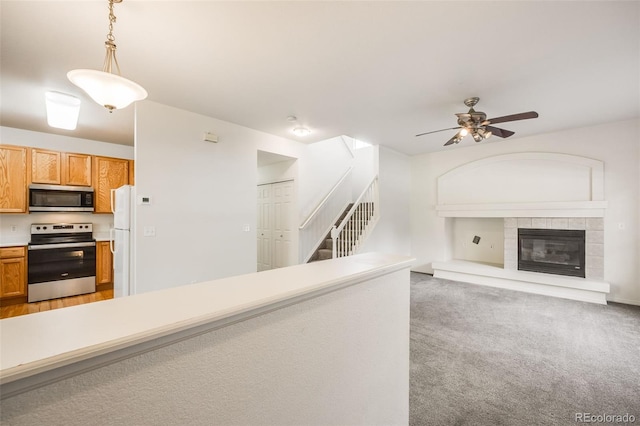 kitchen with light colored carpet, hanging light fixtures, a tile fireplace, ceiling fan, and appliances with stainless steel finishes