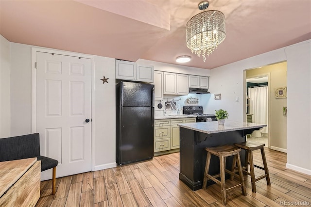 kitchen with light stone countertops, a kitchen bar, light hardwood / wood-style floors, and black appliances