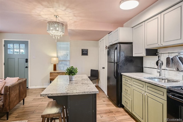 kitchen with a kitchen island, white cabinetry, sink, hanging light fixtures, and light stone countertops