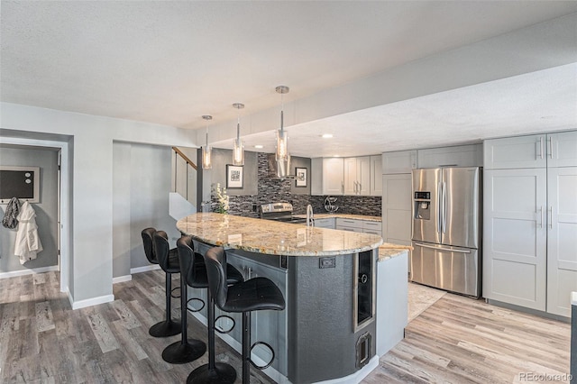 kitchen with backsplash, light wood-type flooring, a kitchen bar, light stone counters, and appliances with stainless steel finishes