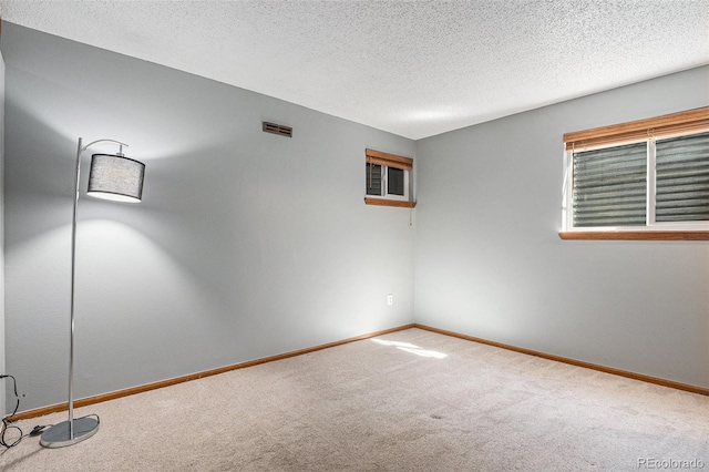 spare room featuring a textured ceiling, carpet, visible vents, and baseboards