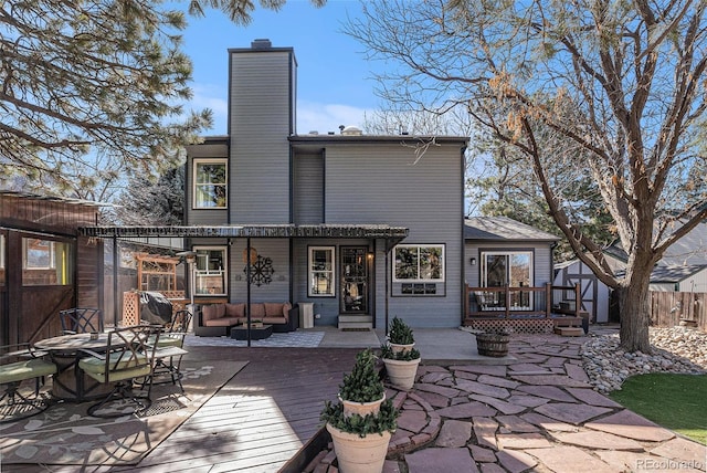 rear view of property with a chimney, a deck, outdoor lounge area, and fence