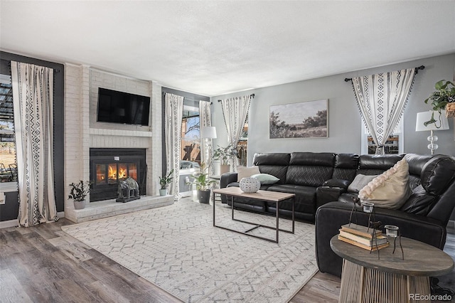 living room with wood finished floors, a brick fireplace, and a healthy amount of sunlight