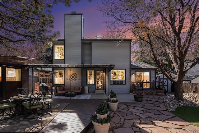 back of property at dusk featuring an outdoor hangout area, a chimney, a deck, and fence