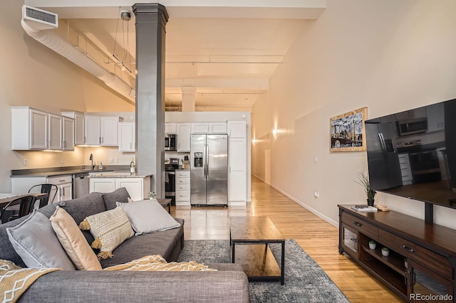 1555 California St Unit 304, Denver, CO 80202 - living room featuring light wood finished floors, a high ceiling, decorative columns, and baseboards