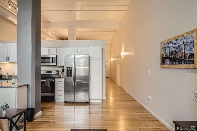 1555 California St Unit 304, Denver, CO 80202 - kitchen with appliances with stainless steel finishes, light wood-style floors, beamed ceiling, white cabinets, and baseboards