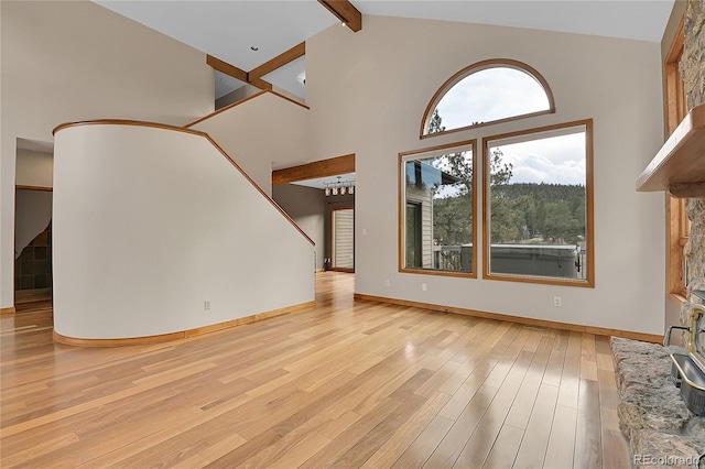 unfurnished living room with baseboards, beamed ceiling, stairs, light wood-style floors, and high vaulted ceiling