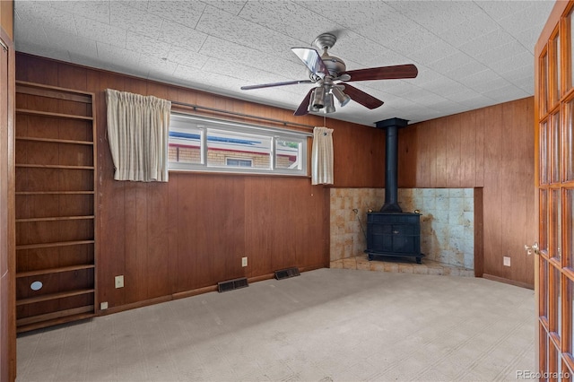 4815 S Pennsylvania St, Englewood, CO 80113 - unfurnished living room featuring wooden walls, built in shelves, a ceiling fan, a wood stove, and carpet