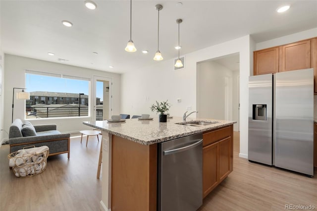 kitchen featuring light stone countertops, appliances with stainless steel finishes, light wood-style floors, and a sink