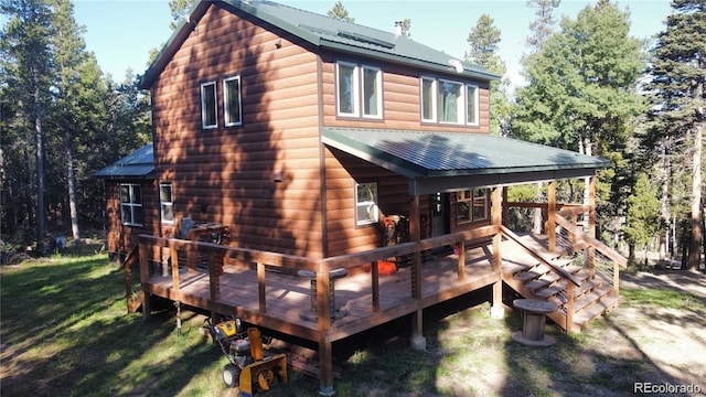 rear view of house with faux log siding, a deck, a yard, and metal roof