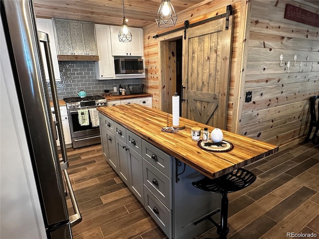 kitchen featuring wood finish floors, gray cabinetry, stainless steel appliances, a barn door, and wooden counters