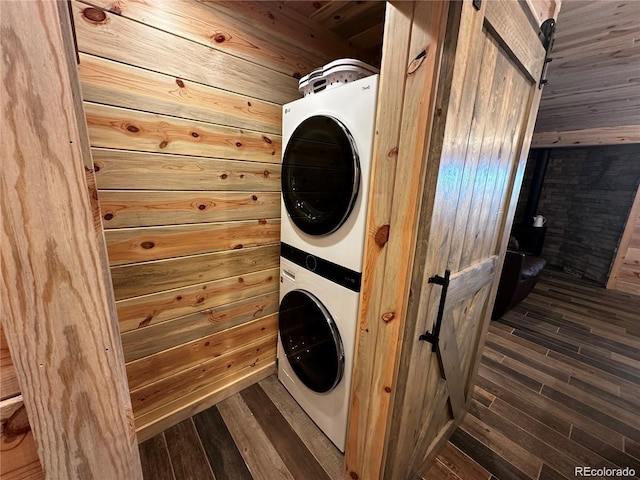 laundry room with stacked washer and dryer, dark wood-style floors, a barn door, wooden walls, and laundry area