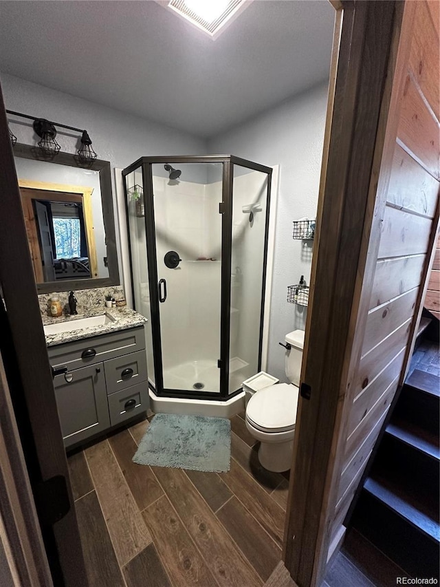 bathroom with visible vents, a shower stall, wood tiled floor, toilet, and vanity