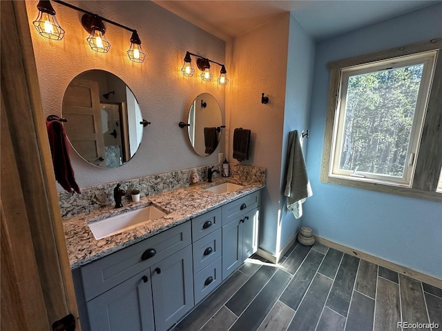 full bathroom with double vanity, baseboards, wood tiled floor, and a sink