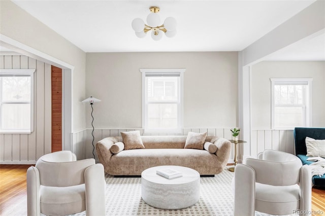 living area with a chandelier, a wainscoted wall, and wood finished floors