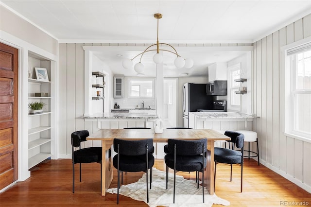 dining room with built in shelves, baseboards, light wood finished floors, and wood walls