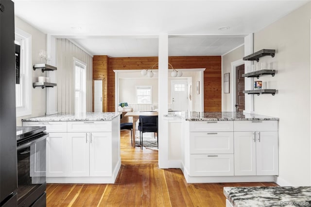 kitchen featuring light wood finished floors, a peninsula, white cabinets, black / electric stove, and open shelves