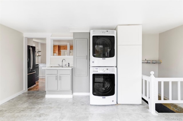 laundry room with stacked washer / dryer, laundry area, baseboards, and a sink