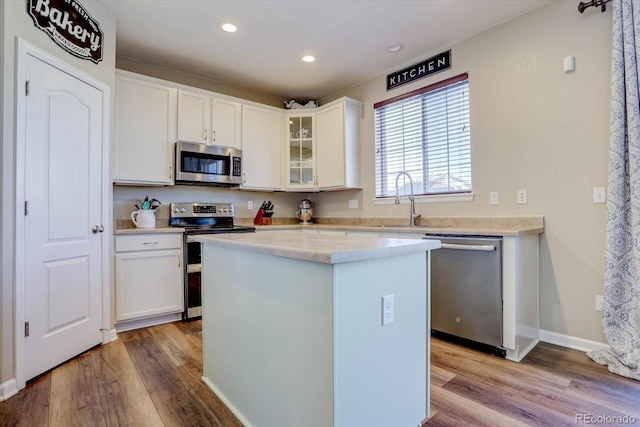 kitchen featuring stainless steel appliances, sink, white cabinetry, light hardwood / wood-style flooring, and a kitchen island