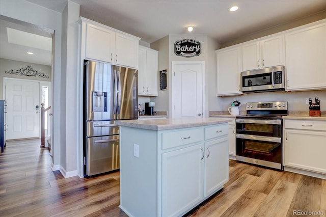 kitchen with stainless steel appliances, white cabinetry, light hardwood / wood-style floors, and a center island