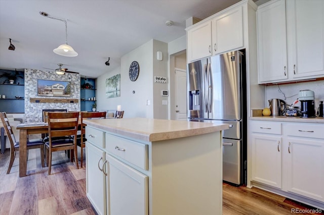 kitchen with white cabinetry, hanging light fixtures, stainless steel fridge, a kitchen island, and built in shelves