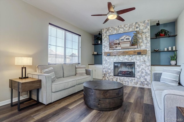 living room with a large fireplace, dark wood-type flooring, and ceiling fan