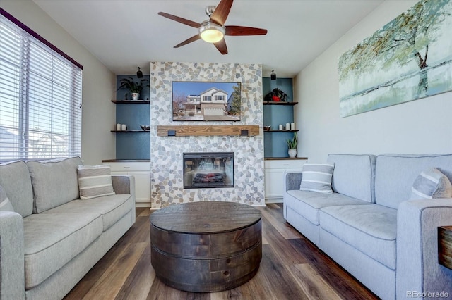 living room featuring a large fireplace, ceiling fan, built in features, and dark wood-type flooring