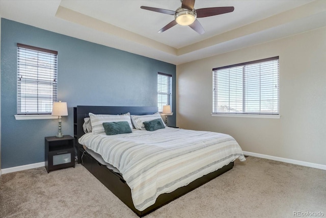 bedroom featuring ceiling fan, light colored carpet, and a tray ceiling