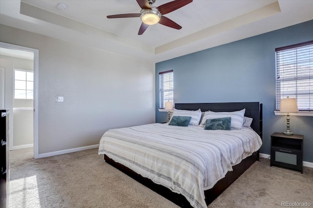 bedroom featuring a raised ceiling, ceiling fan, and light carpet