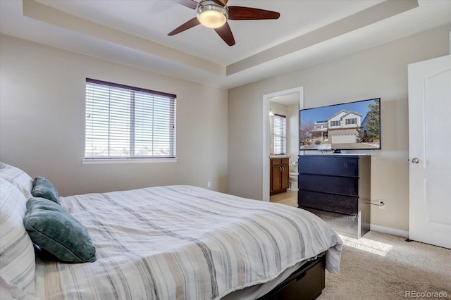 bedroom featuring ensuite bath, a raised ceiling, ceiling fan, and light carpet