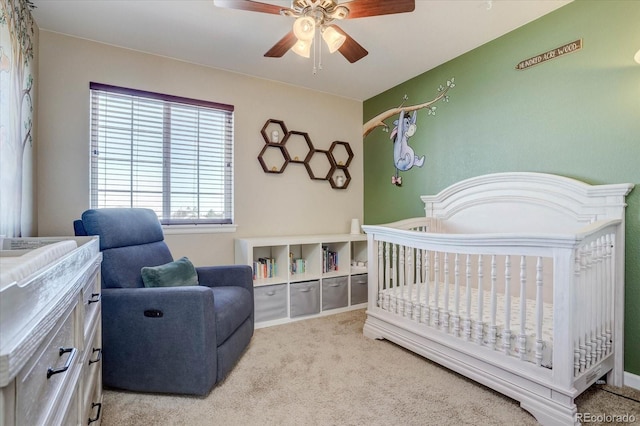 bedroom featuring a crib, light carpet, and ceiling fan