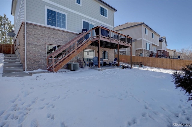 snow covered back of property with central AC and a wooden deck