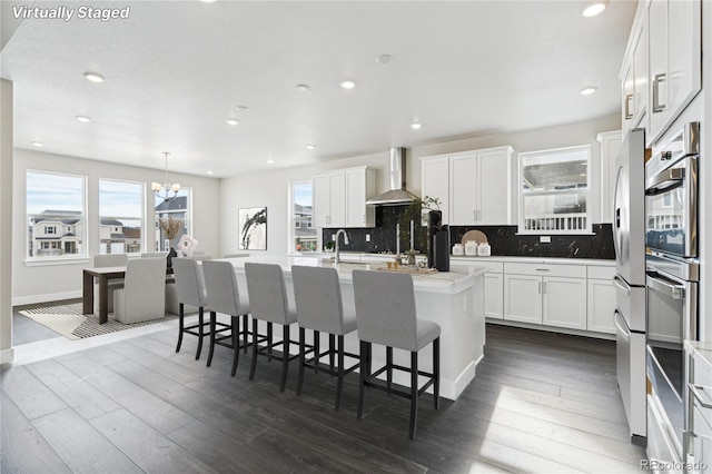 5566 Hickory Oaks Trl, Castle Rock, CO 80104 - kitchen with a chandelier, wall chimney exhaust hood, a center island with sink, decorative backsplash, and recessed lighting
