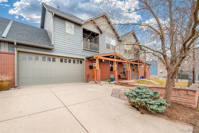 view of front facade with a balcony, roof with shingles, concrete driveway, a garage, and brick siding