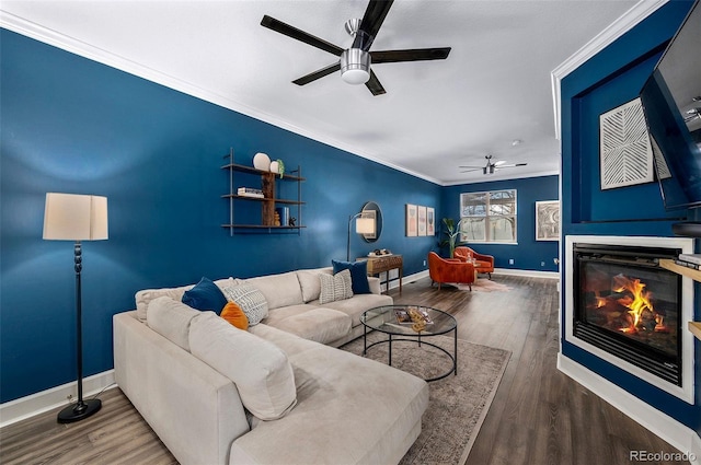 living area featuring crown molding, baseboards, wood finished floors, a glass covered fireplace, and a ceiling fan