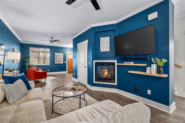 living area with a glass covered fireplace, crown molding, wood finished floors, and ceiling fan