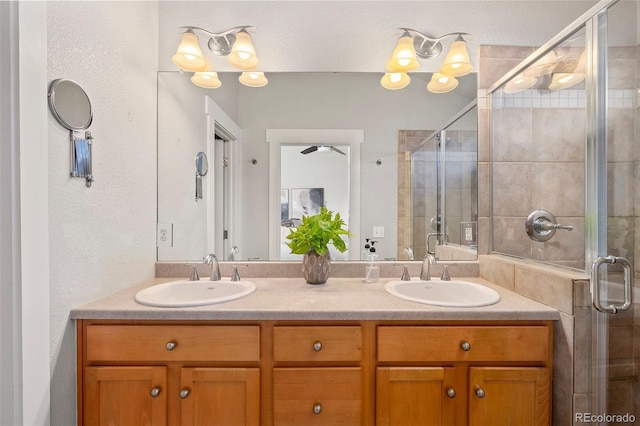 full bathroom with a textured ceiling, a shower stall, double vanity, and a sink