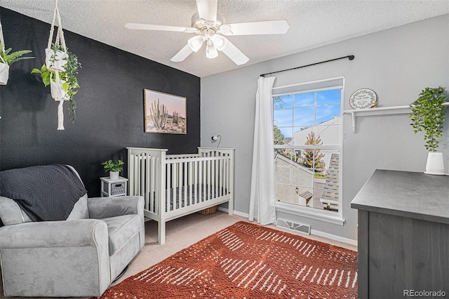 bedroom with a crib, a textured ceiling, carpet floors, and ceiling fan