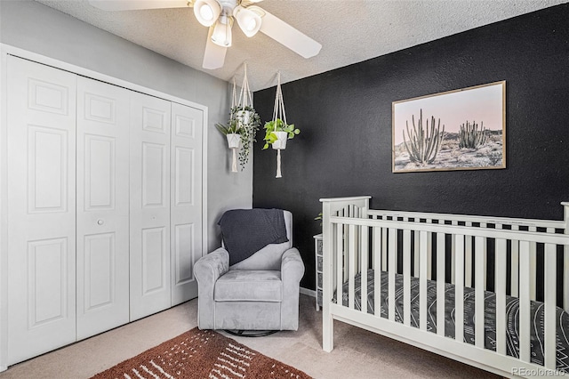 carpeted bedroom featuring a textured ceiling, a closet, a nursery area, and ceiling fan