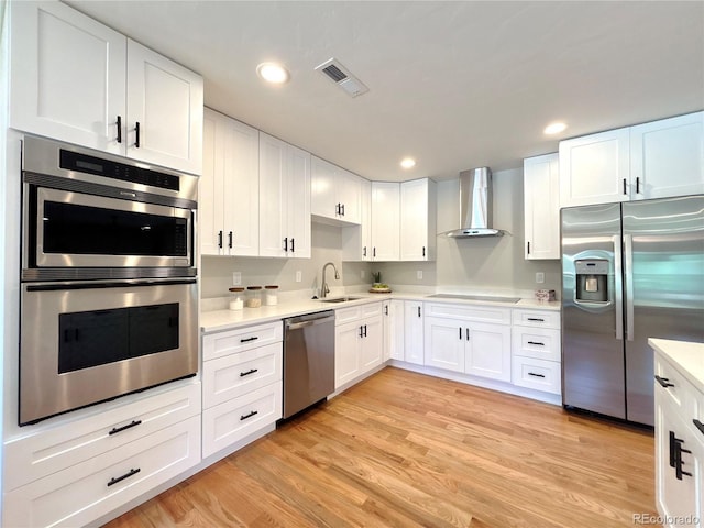 9451 E Evans Pl, Denver, CO 80231 - kitchen featuring appliances with stainless steel finishes, wall chimney range hood, light countertops, white cabinetry, and light wood finished floors