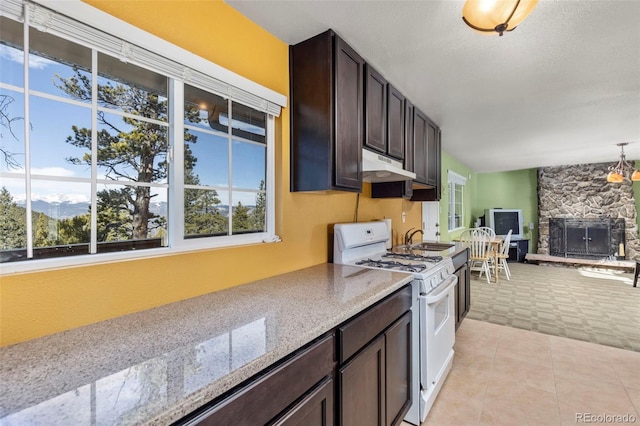 kitchen featuring light stone countertops, dark brown cabinetry, a mountain view, a stone fireplace, and white gas stove