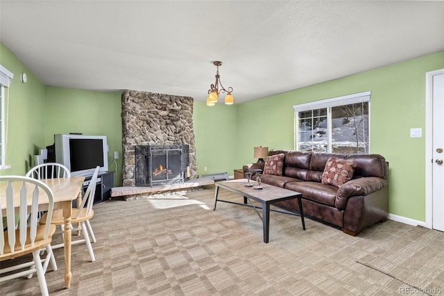 living room featuring a stone fireplace, light colored carpet, a baseboard heating unit, and an inviting chandelier